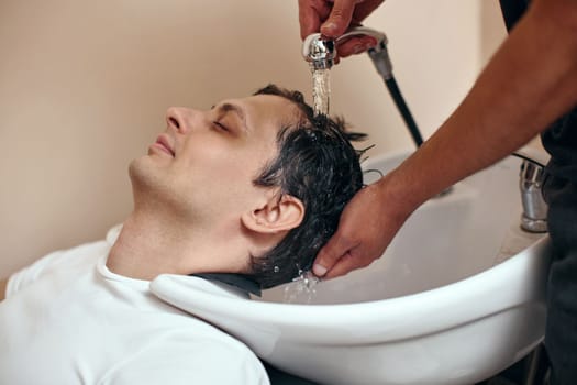 Barber washing hair of caucasian man in barber shop
