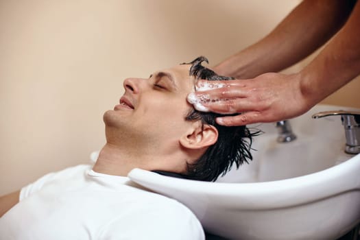 Barber washing hair of caucasian man in barber shop