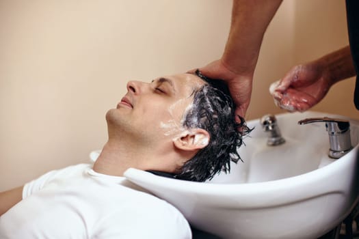 Barber washing hair of caucasian man in barber shop