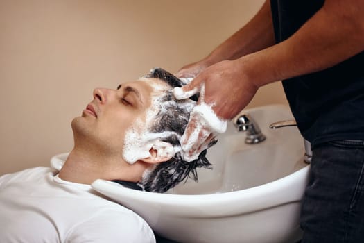Barber washing hair of caucasian man in barber shop