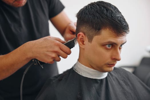 cut hair with electric shearer machine on handsome caucasian man in barber shop.
