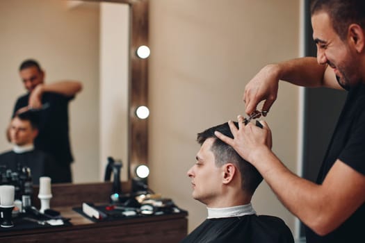 Hairstylist serving handsome bearded man in barber shop.