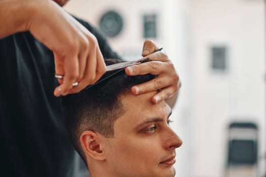 hairdresser does haircut for caucasian man in barber shop. close-up