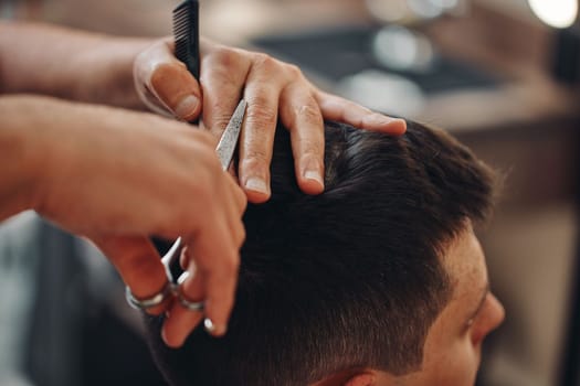 hairdresser does haircut for caucasian man in barber shop. close-up