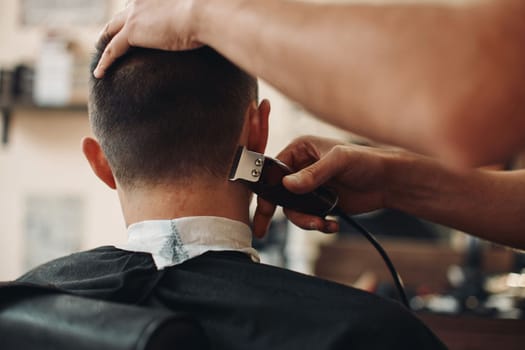 Rear view of barber trim hair with clipper on handsome caucasian man in barber shop.