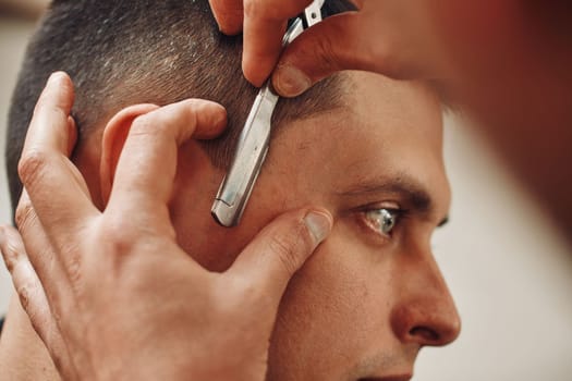 Barber shaving bearded man with razor in barber shop. close-up