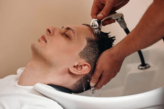 Barber washing hair of caucasian man in barber shop