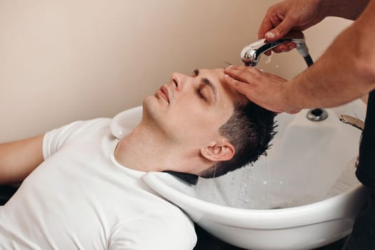 Barber washing hair of caucasian man in barber shop