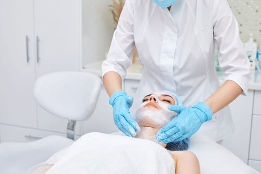 beautician applies the mask to the face of beautiful young woman in the spa salon. facial skin care concept.