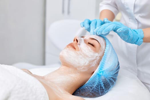 beautician applies the mask to the face of beautiful young woman in the spa salon. facial skin care concept.