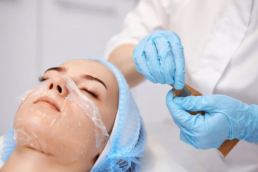 beautician in blue gloves opens package with sterilized instruments and woman on the couch in the spa salon.
