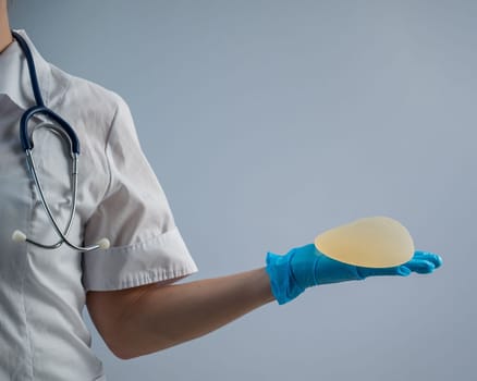 Female doctor aesthetic surgeon holding a breast implant on a white background