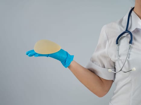 Female doctor aesthetic surgeon holding a breast implant on a white background