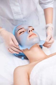 beautician removing blue alginate mask from face of beautiful woman in the spa salon. spa treatments