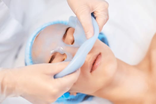 beautician removing blue alginate mask from face of beautiful woman in the spa salon. spa treatments