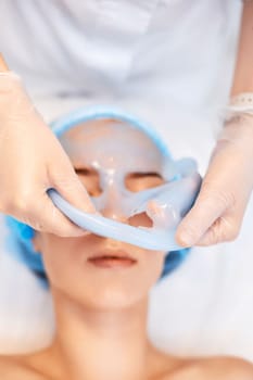 beautician removing blue alginate mask from face of beautiful woman in the spa salon. spa treatments