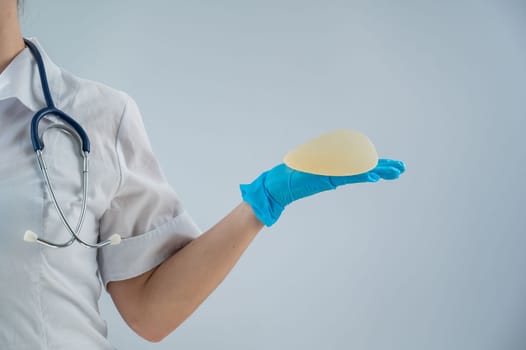 Female doctor aesthetic surgeon holding a breast implant on a white background