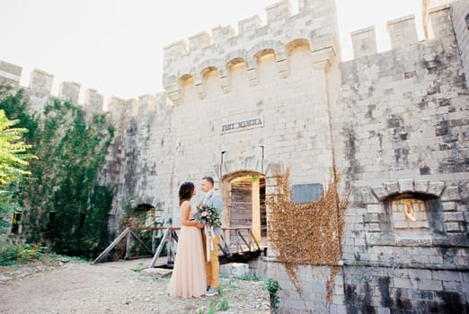 Groom hugs bride near the wooden bridge to the entrance to Mamula Fort. High quality photo