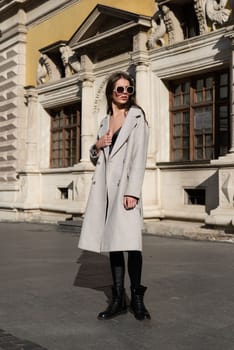 Street style, autumn, spring fashion concept: fashionable woman wearing luxury beige coat, sunglasses, wide leg black leggings, ankle bots. Full length shot on beige background.