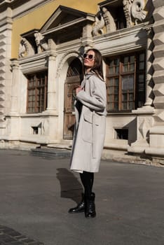 Street style, autumn, spring fashion concept: fashionable woman wearing luxury beige coat, sunglasses, wide leg black leggings, ankle bots. Full length shot on beige background.