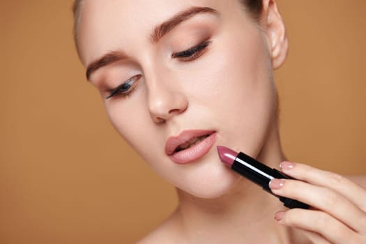beautiful woman applying pink lipstick on beige background, close-up