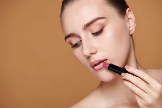beautiful woman applying pink lipstick on beige background