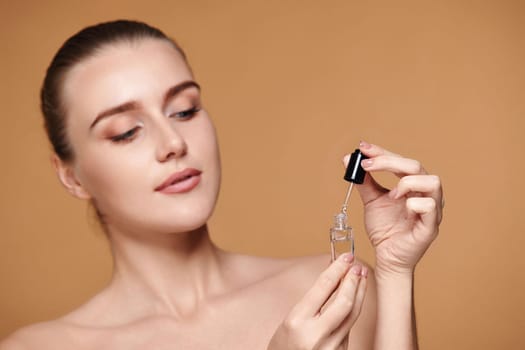 beautiful woman holding bottle with serum for skin care on beige background