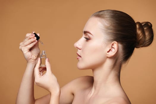 attractive woman holding bottle with serum for skin care on beige background