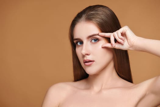 Beautiful healthy woman with perfect skin check the line of eyebrows and eyes without wrinkles on beige background. Face lifting concept.
