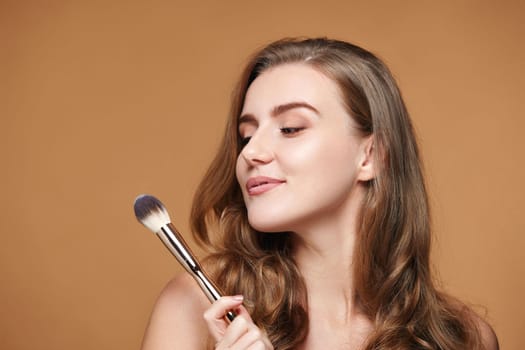 beautiful curly woman with make-up brush for powder on beige background.