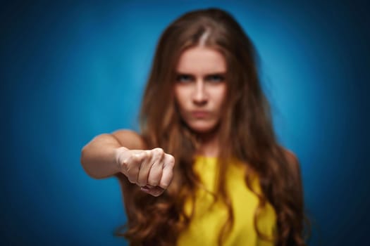 Ukrainian woman in yellow t-shirt protesting against Russian military invasion in Ukraine on blue background. Angry gesture. focus on fist