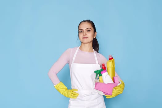 pretty caucasian woman in gloves holding bucket with cleaning supplies isolated on blue background.