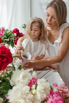 A little blonde girl with her mom on a kitchen countertop decorated with peonies. The concept of the relationship between mother and daughter. Spring atmosphere.