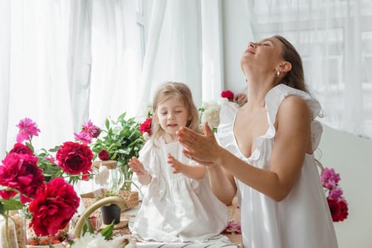 A little blonde girl with her mom on a kitchen countertop decorated with peonies. The concept of the relationship between mother and daughter. Spring atmosphere.