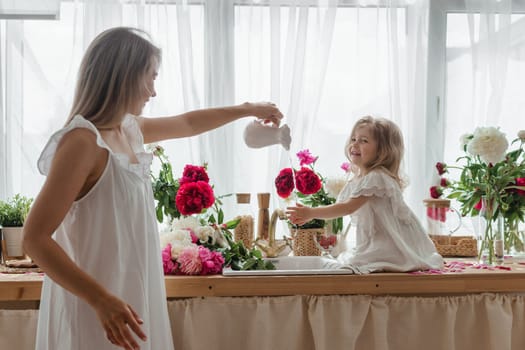 A little blonde girl with her mom on a kitchen countertop decorated with peonies. The concept of the relationship between mother and daughter. Spring atmosphere.