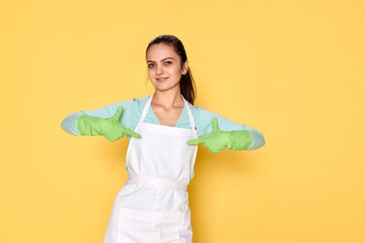 smiling caucasian woman in gloves pointing oneself with fingers on yellow background. cleaning