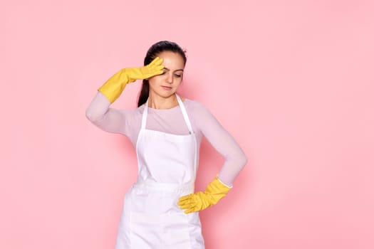 tired woman in gloves and cleaner apron on pink background