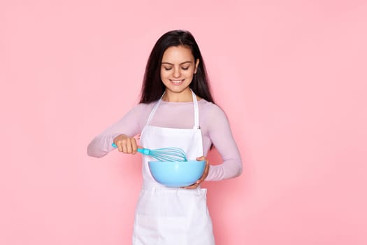 happy housewife woman holding whisk and bowl on pink background