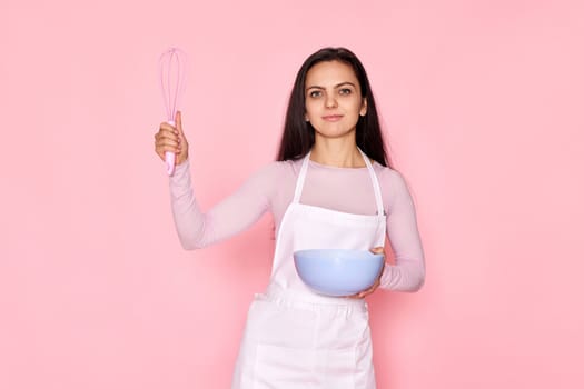 beautiful cooker woman using bowl and whisk on pastel pink background