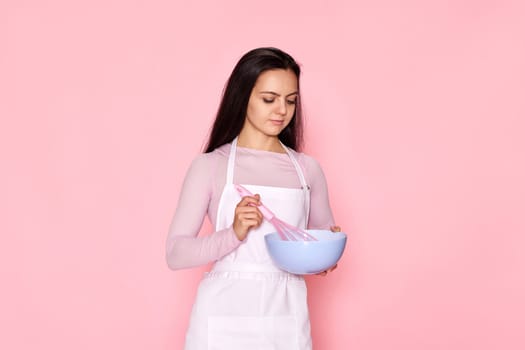 beautiful chef woman using bowl and whisk on pink background