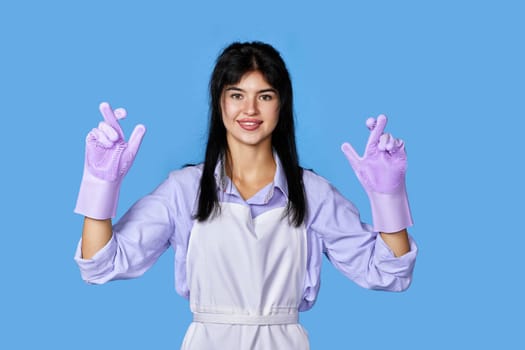 caucasian woman in rubber gloves with finger crossed gesture isolated on blue background. cleaning
