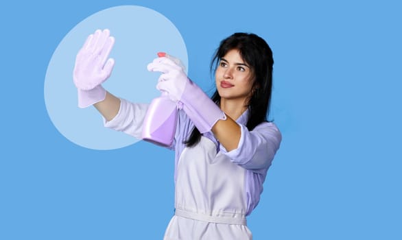 young confident woman in purple rubber gloves and cleaner apron cleaning glass with detergent sprayer on blue background.