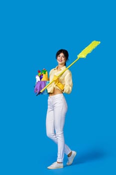 happy caucasian housewife girl in rubber gloves housekeeping and cleaning with mop and holding bucket of detergents on blue background. Full length