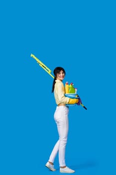 smiling girl in rubber gloves housekeeping and cleaning with mop and holding bucket of detergents on blue background. Full length