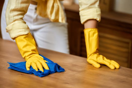brunette woman in yellow gloves using a rag while cleaning furniture at home