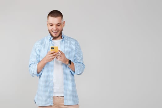 happy handsome bearded man in blue t-shirt messaging with mobile cell phone