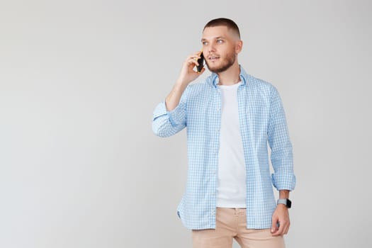 Handsome young man using cell phone while standing against gray background.