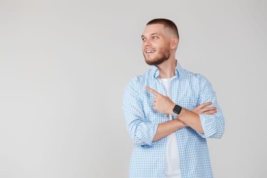 Young handsome bearded man pointing to the side to present a product isolated on gray background