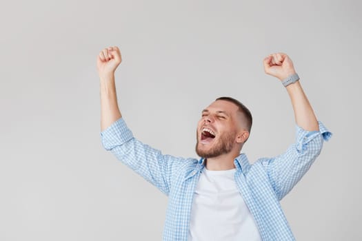 amazed young man celebrating victory on gray background.