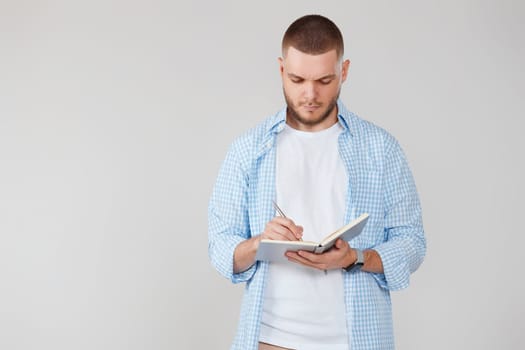 handsome man in casual blue shirt writing note in notebook